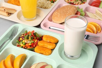 Plastic trays with tasty food, milk and orange juice on grey table, closeup. School lunch