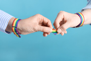 LGBT concept. Women in rainbow wristbands with heart shaped pin on light blue background, closeup