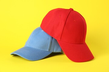 Red and light blue baseball caps on yellow background, closeup. Mockup for design