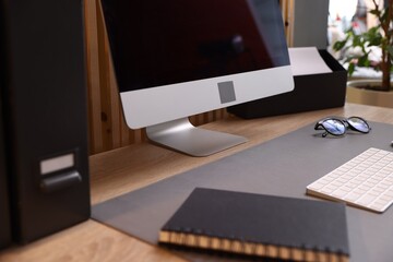 Stylish workplace with wooden desk, computer, notebook and glasses in office, closeup