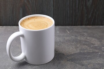Aromatic coffee in cup on grey textured table against dark wooden background, closeup. Space for text