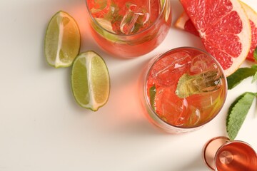 Tasty cocktail with ice cubes, lime and grapefruit on white table, flat lay. Space for text