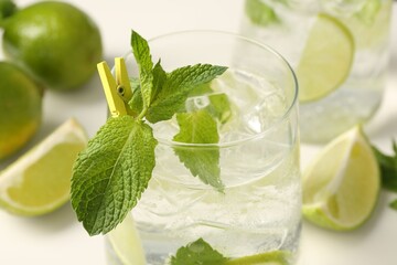 Tasty cocktail with lime and ice cubes on white table, closeup