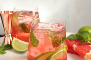 Tasty cocktail with ice cubes, lime and grapefruit on white table, closeup