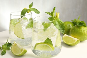 Tasty cocktail with lime and ice cubes on white table, closeup