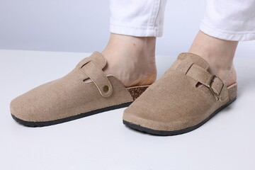 Woman in stylish beige slippers on light floor against grey background, closeup