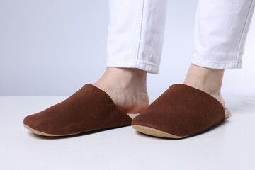Woman in soft brown slippers on light floor against grey background, closeup