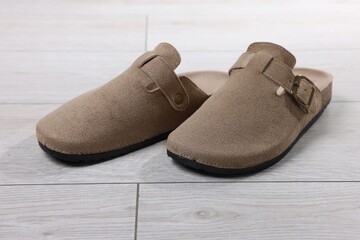 Stylish beige slippers on light wooden floor, closeup