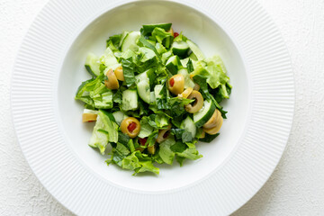 Mediterranean salad with green olives on white plate in close-up