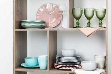 Shelving unit with different dishware and glasses near white wall indoors