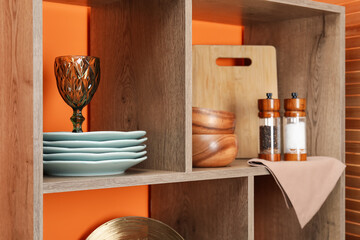 Shelving unit with different dishware and glass near orange wall indoors