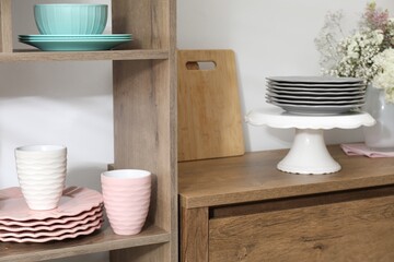 Shelving unit with different dishware and cups near white wall indoors