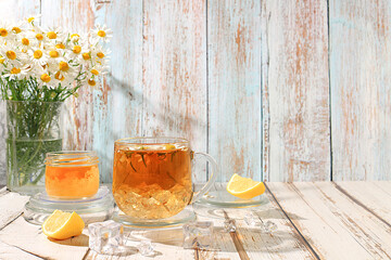 Chamomile tea or infusion with lemon, honey and ice in transparent glasses with natural small...