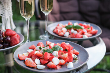 Strawberry, mozzarella and tomato salad and champagne flutes on glass garden table. Perfect for displaying summer recipes and gourmet dishes