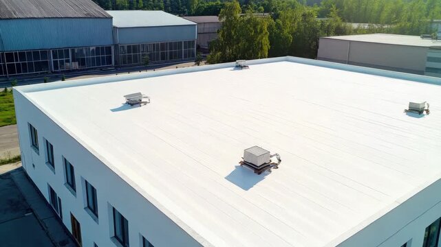 An aerial view of a modern warehouse with a flat roof. Empty and spacious, showing solar panels on the roof. The building is surrounded by trees.