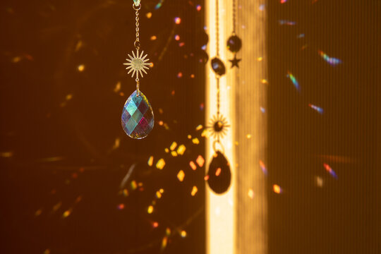 Glass suncatcher with metal golden chains, shining in sunlight and reflecting the rainbow on a yellow background