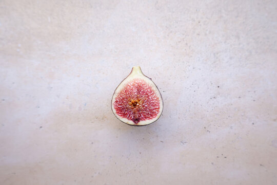 Higo morado partido por la mitad visto desde arriba. Imagen minimalista, textura org&aacute;nica, fondo neutro. Fotograf&iacute;a cenital de fruta natural y saludable.