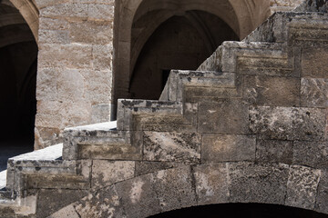 Historic stone courtyard with arched staircases, ancient sculptures in a Mediterranean old town