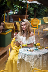 beautiful girl with glass of lemon colored lemonade in hand in cafe on summer day
