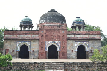 Fototapeta premium Isa Khan’s Tomb, built in red sandstone, is a pre-Mughal masterpiece with intricate lattice work, arched verandas, and lush garden surroundings—radiating timeless charm and architectural grace.
