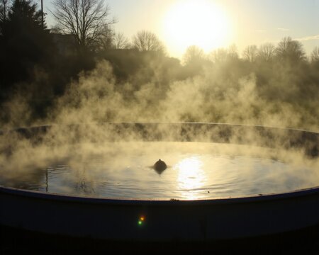 Early sunlight breaks through mist over a calm circular anaerobic pond. Anaerobic reservoir with warm water surface flowing gently and radiant fog illuminated by sun rays.