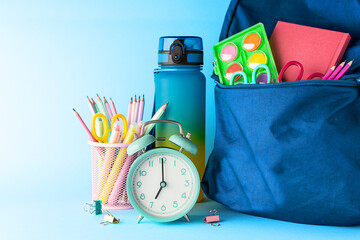 Stationery supplies, backpack and alarm clock on light blue background close up. Back to school...