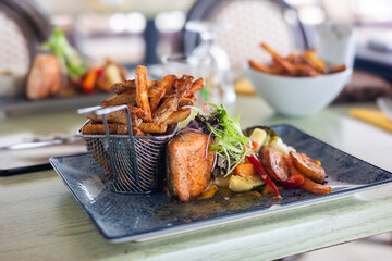 Grilled Salmon with French Fries and Sautéed Vegetables on a Black Plate