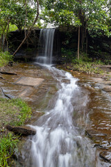 A peaceful view of Than Nam Sai waterfall, a small clear stream in Phu Pha Yon National Park, Thailand. Surrounded by green trees, perfect for nature, travel, and landscape concepts.