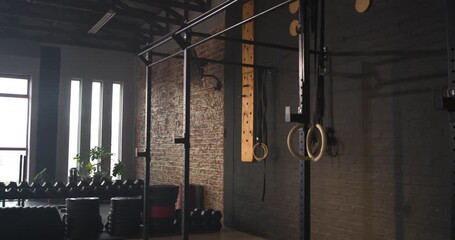 Camera pulling back from rings panning right revealing rig dumbbells mats in studio, copy space