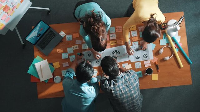 Top view of business team write graphic logo on meeting table with colorful sticky notes and design while explain idea. Project manager sharing idea and explain concept art to smart team. Symposium.
