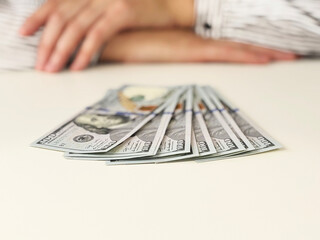 Dollar paper bills on white table with blurred woman in background. Close-up of US currency,...