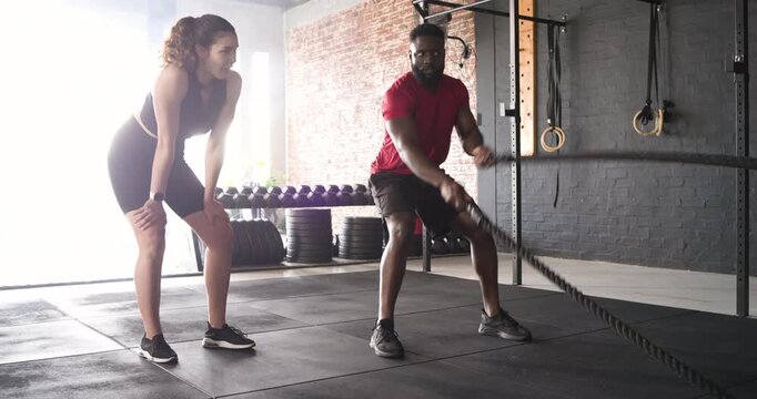 Trainer demonstrating battle rope waves guiding female client waves gaining power in gym