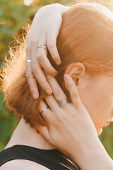 Red-haired woman with multiple silver rings, holding her head in a sunflower field