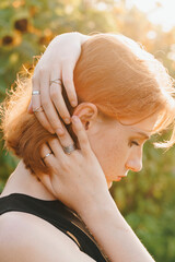 Red-haired woman adjusting her hair, wearing silver rings in sunlight