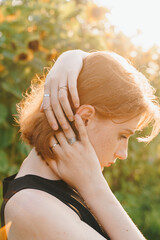 Red-haired woman adjusting her hair, wearing silver rings in sunlight