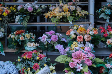 Colorful artificial flower arrangements displayed on shelves at a grave decoration stand, typically used for memorial purposes.

