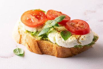 Fresh homemade caprese sandwich with avocado paste, mozzarella cheese, cherry tomatoes, fresh aromatic basil leaves and spicy hot oil close up. Healthy homemade food concept.
