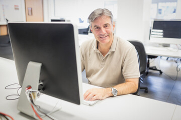 All-in-one desktop monitor is displaying blank screen on desk in open-plan office, showing cables