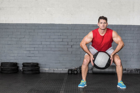 Fototapeta Medicine ball being held at chest height while squatting in gym with weight plates and dumbbells