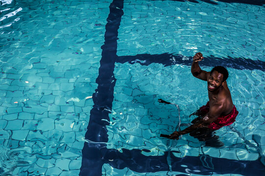 Fototapeta Man standing waist-deep in turquoise lap pool, raising fist near dark lane stripe
