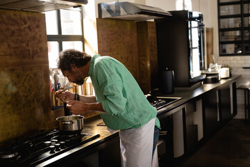 Stainless steel pot simmering on gas cooktop in kitchen with backsplash, utensils, and window light