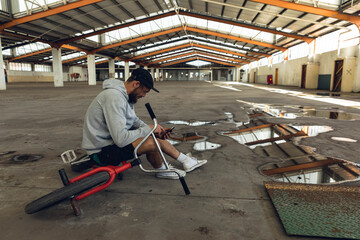 Red BMX bicycle resting on concrete warehouse floor with puddles reflecting orange steel trusses