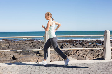 Jogger jogging along paved seaside promenade past white railing, with rocky shore and ocean horizon