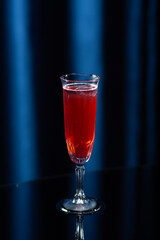 A tall glass filled with a bright red cocktail with ice cubes, placed on a reflective black surface...