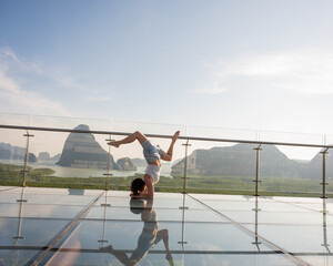 Caucasian woman doing forearm stand on glass bridge among mountains. 