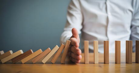 Preventing Domino Effect: A person's hand halting the cascading collapse of a row of wooden blocks, symbolizing risk management and strategic intervention.