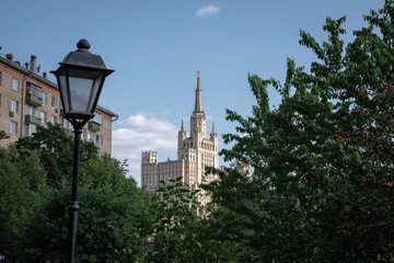 Urban scene featuring a tall building behind green foliage and a streetlight under a clear blue...