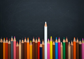 White pencil standing out from a crowd of colored pencils on a blackboard. Concept for leadership, uniqueness, and individuality. Top view with copy space.