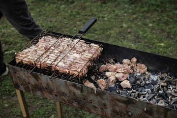 Close-up of skewers and meat cooking on a charcoal grill outdoors. The grilling process shows...