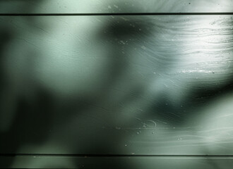 Close-up of a green painted wooden surface made of horizontal panels. The image features fine wood grain textures, light reflections, subtle water stains, and abstract shadow patterns.